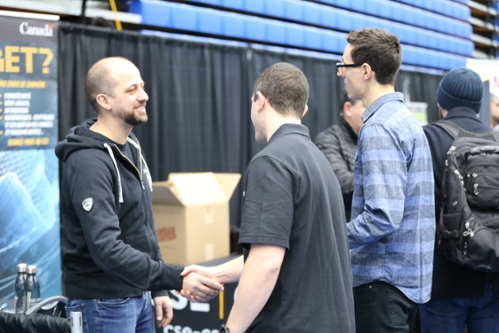 Recruiting talking to two students while shaking one of the student's hands at job fair.