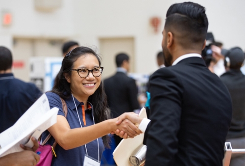 Recruiter with glasses shaking the hand of a student wearing a suit at an Engineering Reverse Career Fair