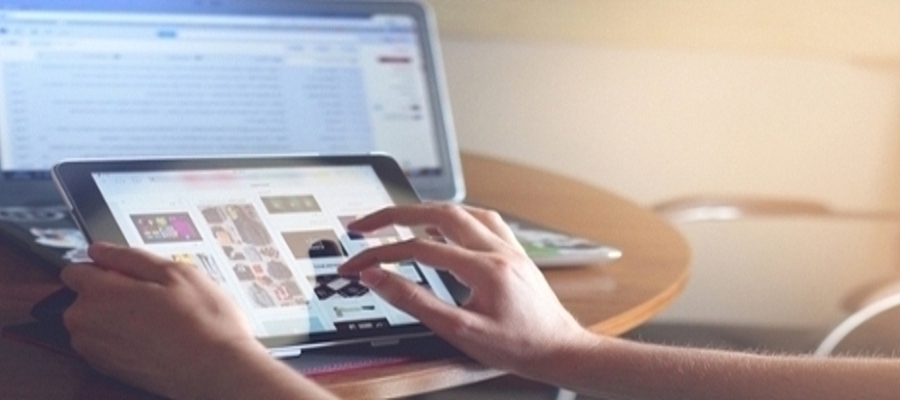 Close up of a person's hands scrolling iPad with a laptop in the background