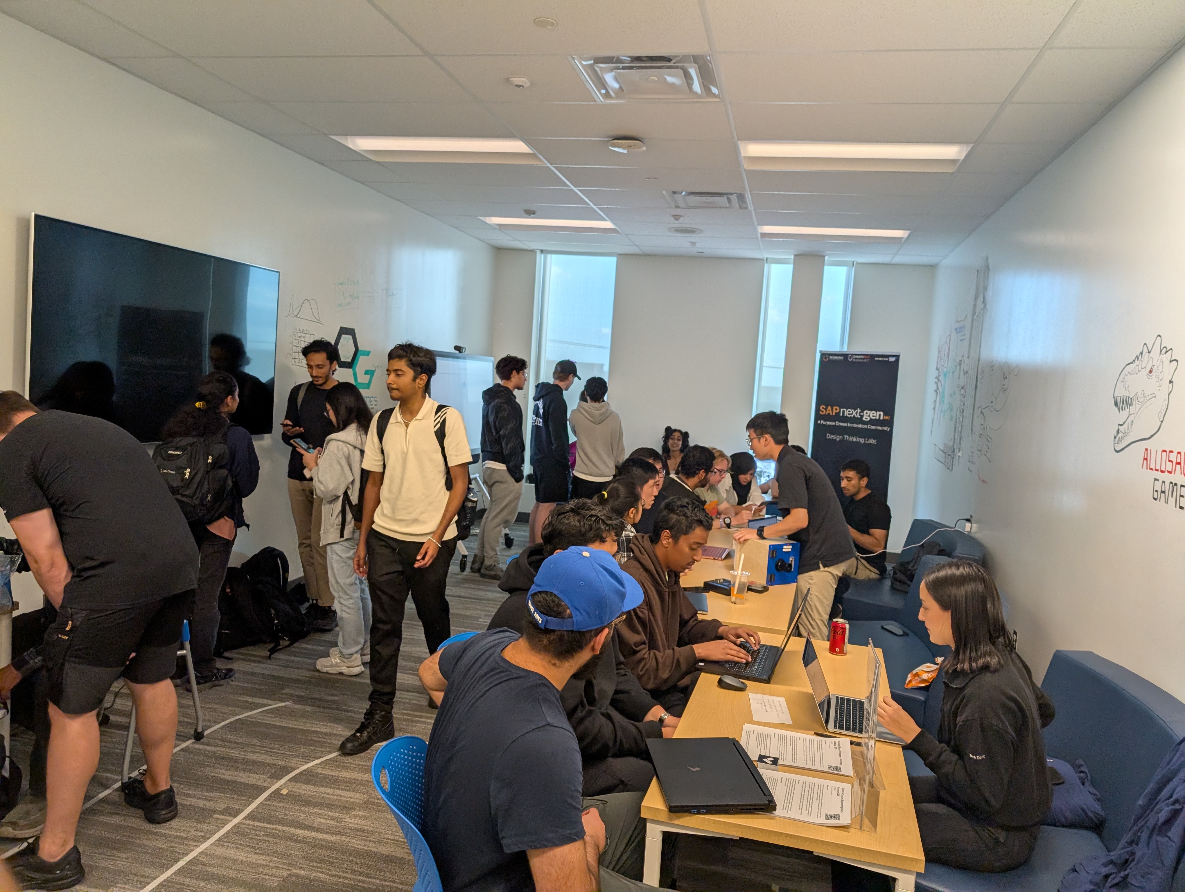 A collaborative workspace filled with students working on laptops and discussing ideas in a modern classroom setting.