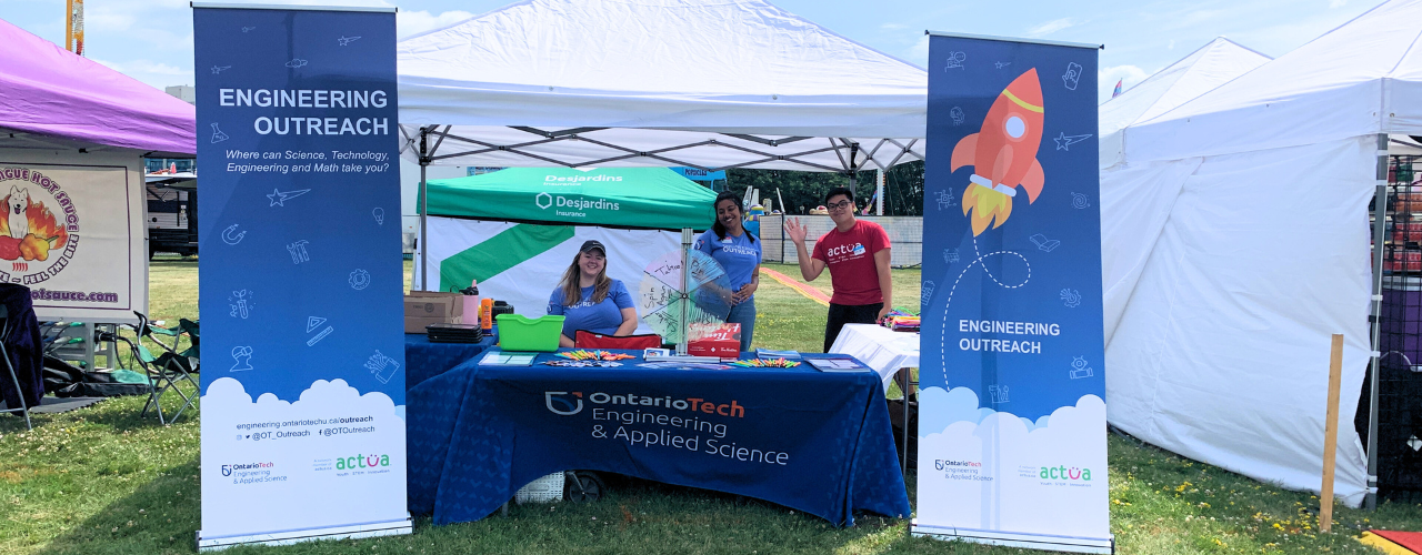 Engineering Outreach Instructors at an event booth set up outside on a sunny day