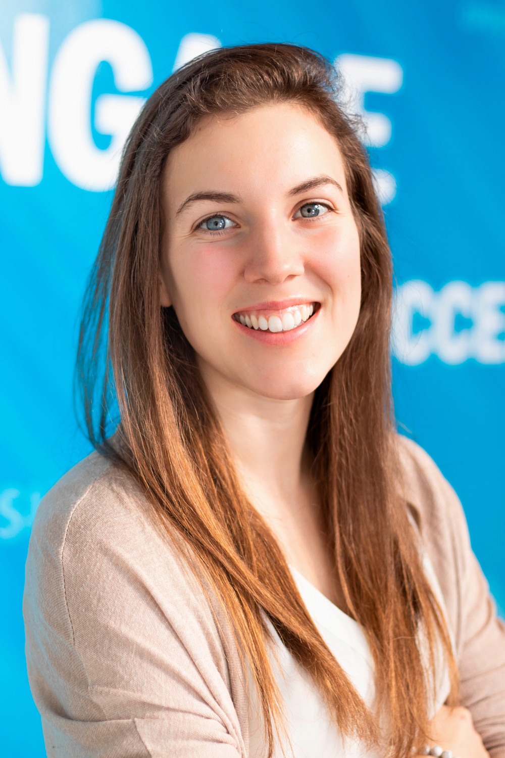 Smiling woman with long brown hair and a warm expression, set against a vibrant blue background.