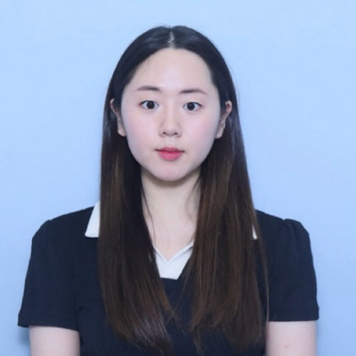 A professional headshot of a young woman with long, straight hair, wearing a black blouse with a white collar, set against a light blue background.