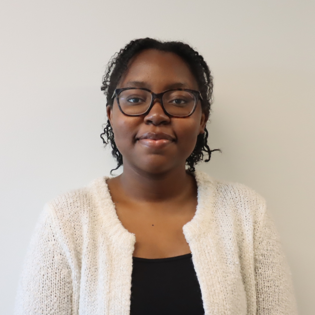 A young woman with curly hair wearing glasses and a light cardigan, smiling softly against a neutral background.