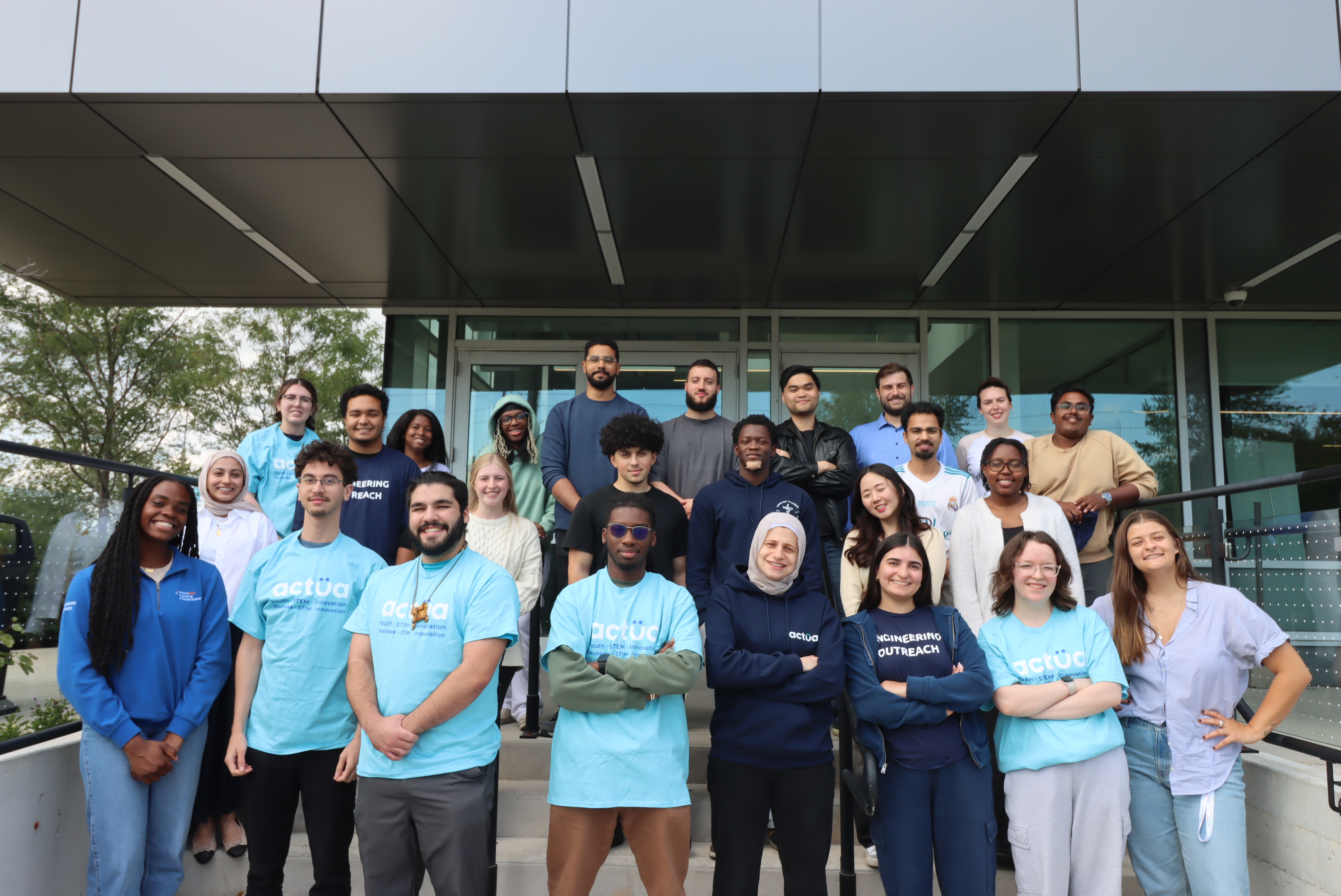Group photo of a diverse team of young adults standing outside a modern building, dressed in casual attire.
