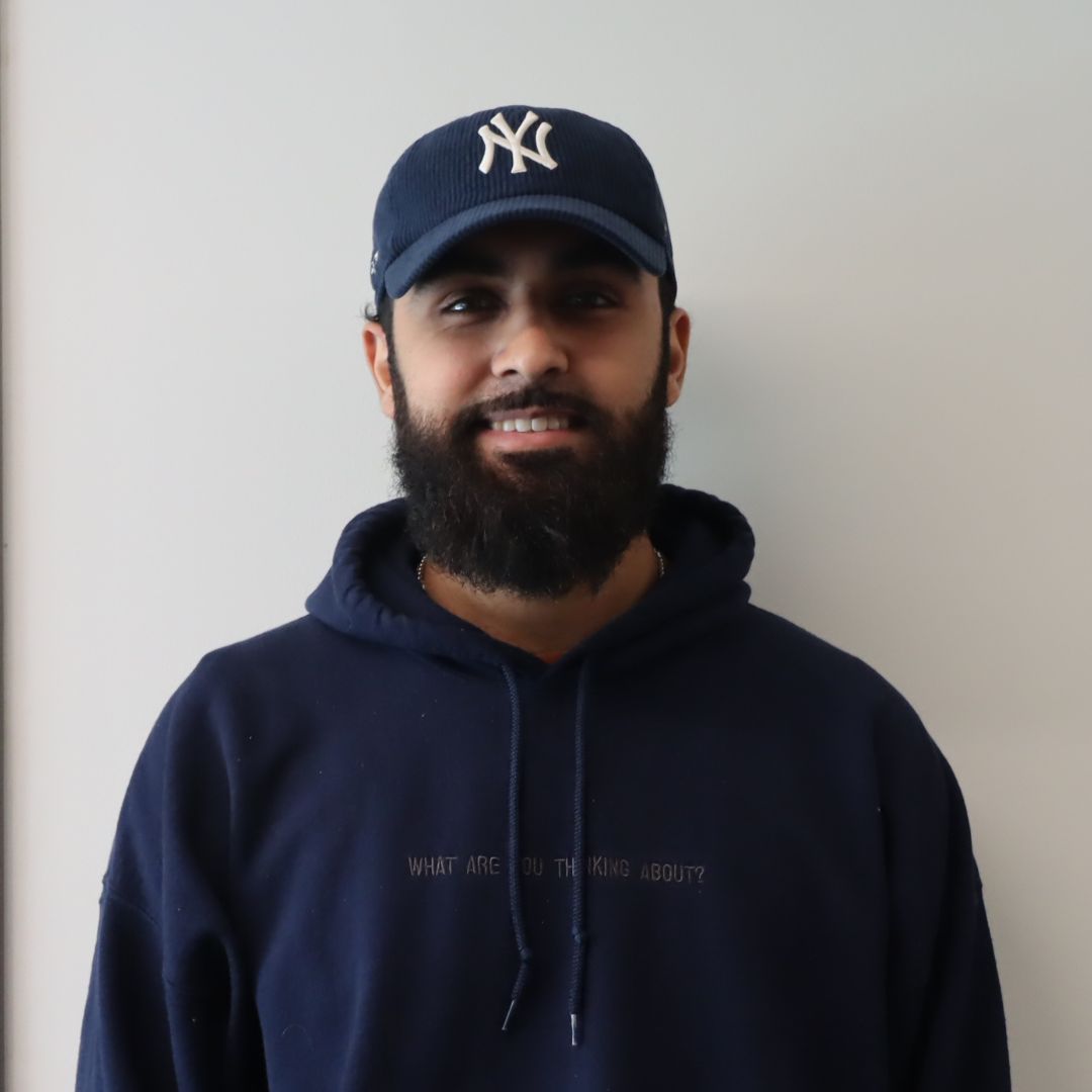 A young man with a beard wearing a navy hoodie and a New York Yankees cap.