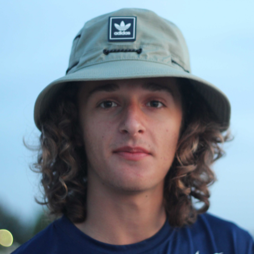 A young man with curly hair wearing a beige bucket hat and a navy blue shirt.