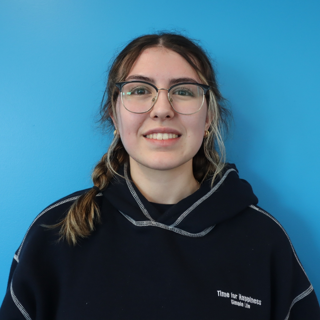 A smiling young woman with glasses and a braid, wearing a dark sweatshirt against a blue background.
