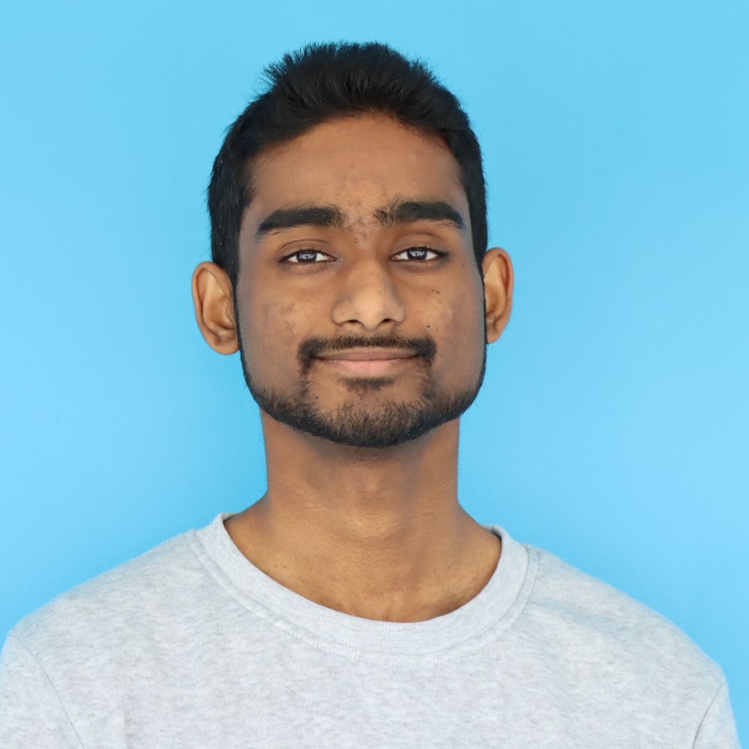 A young man with a slight smile, wearing a light gray sweatshirt against a bright blue background.