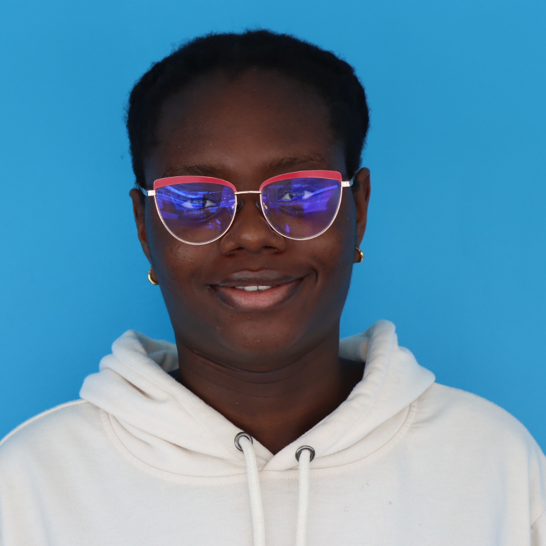 A smiling young woman wearing colorful glasses and a white hoodie against a bright blue background.