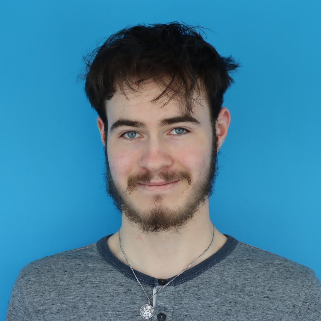 A smiling person with a beard and casual attire against a bright blue background.
