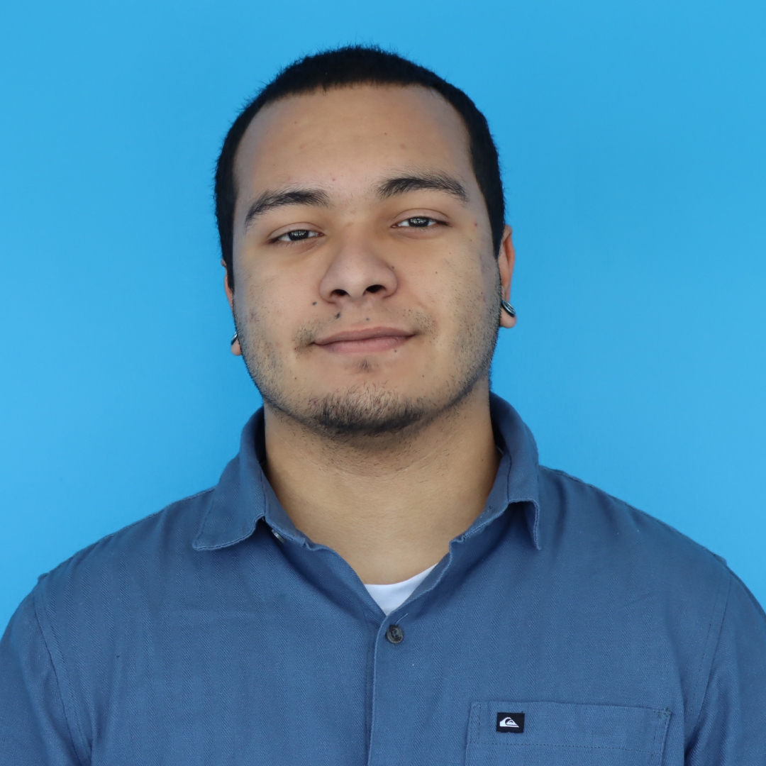 A young man with a slight smile, wearing a blue collared shirt, set against a bright blue background.