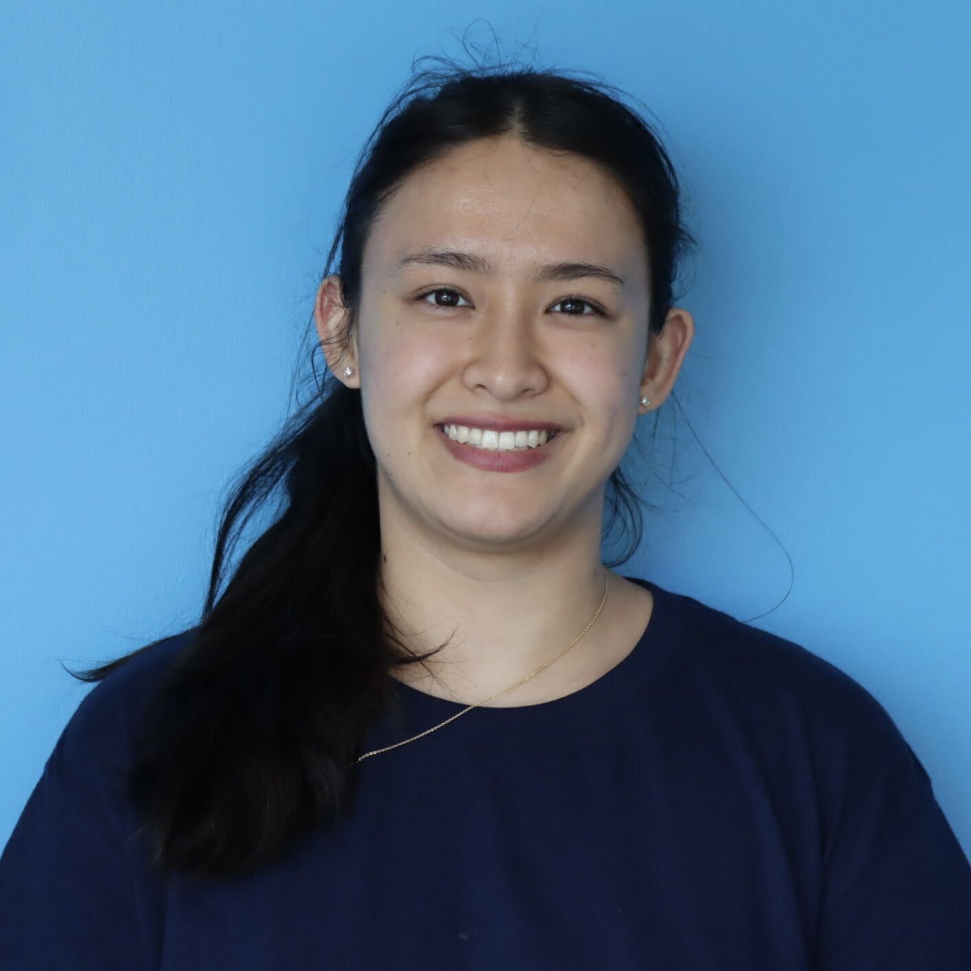 Smiling woman with long dark hair in a navy top, posed against a light blue background.