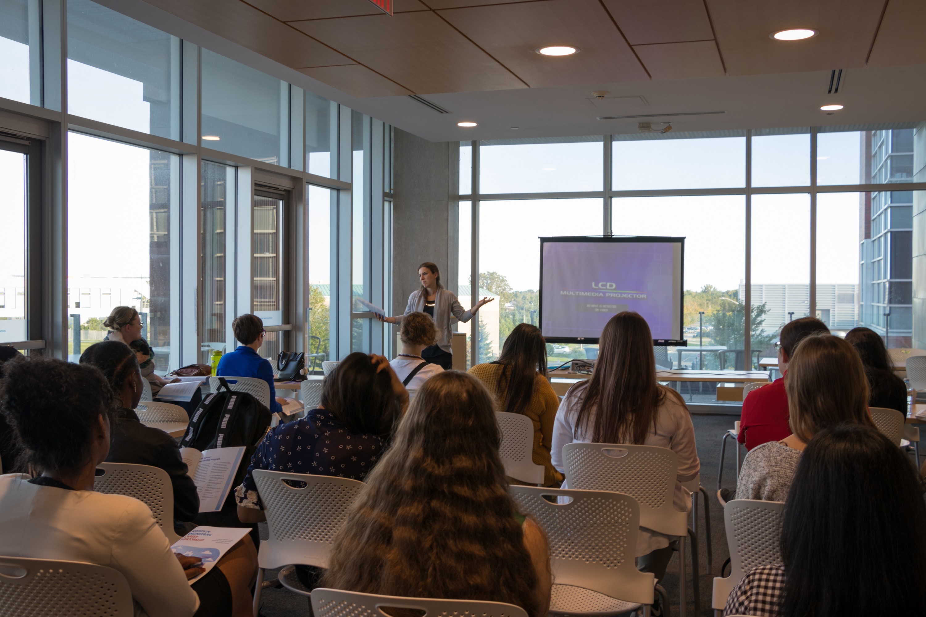 A group of students in the audience as a presenter stands on a podium at the front of the room.
