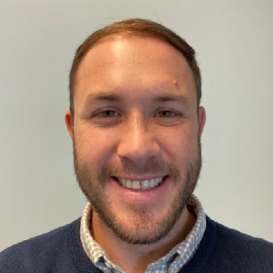 Headshot of a smiling man with a short beard, wearing a blue sweater and a collared shirt.