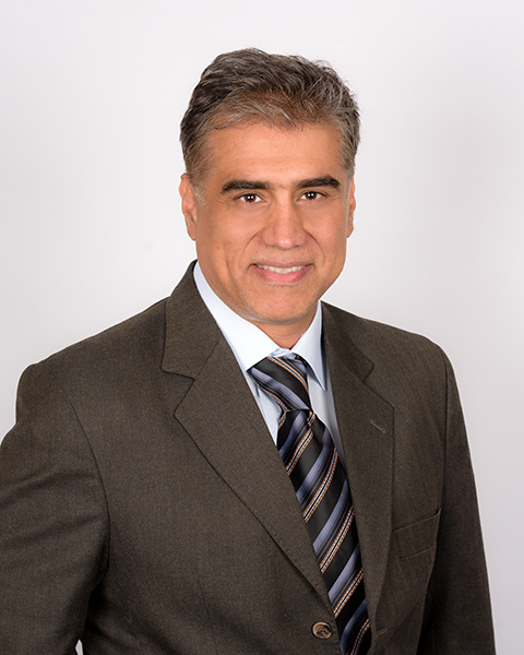 Professional headshot of a man with curly hair, wearing a black suit and tie.