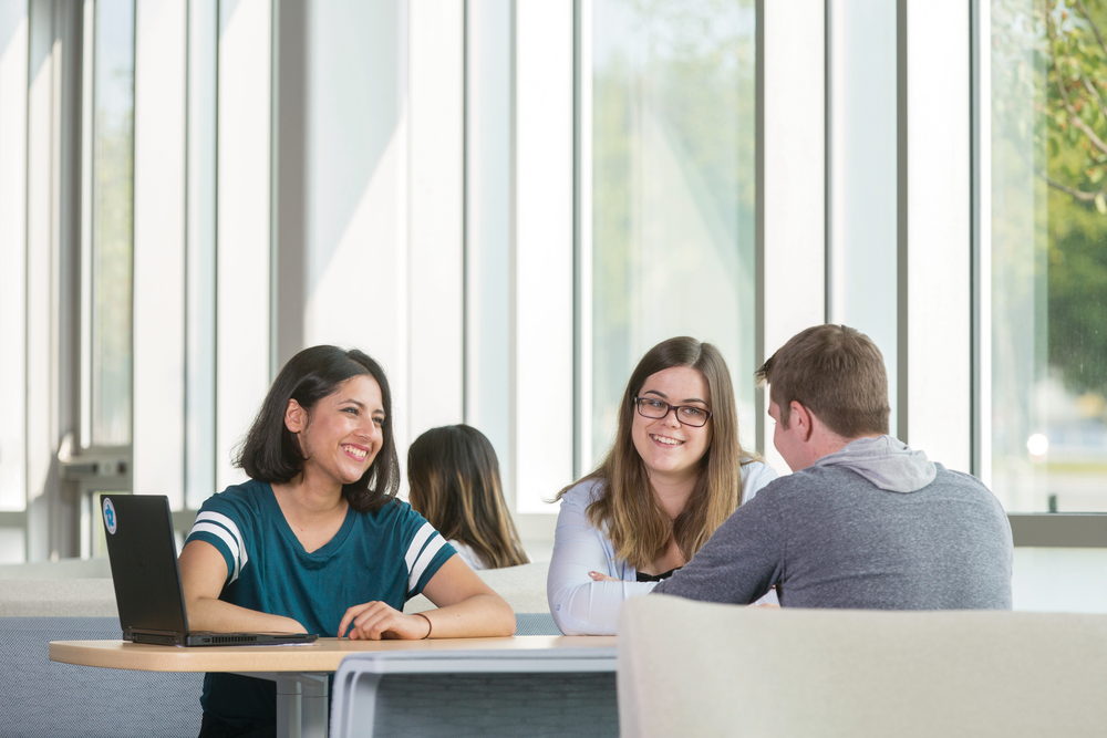 Three students studying at a table in a large open space.