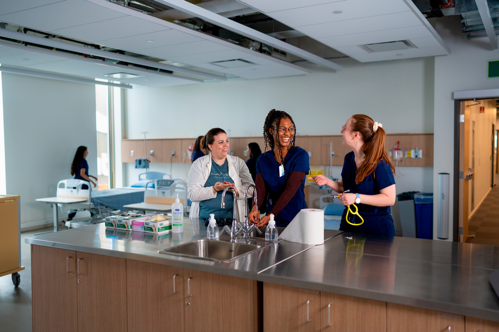 Two nursing students and a staff member chatting in the nursing lab.