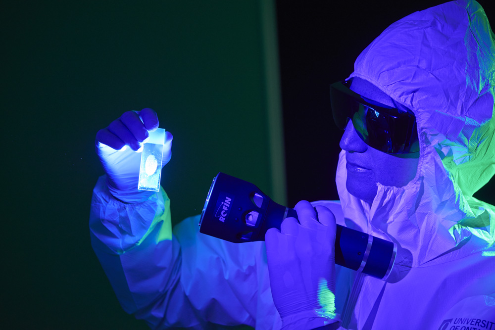 Forensic scientist shining an alternate light source on a glass slide to visualize a fingerprint.