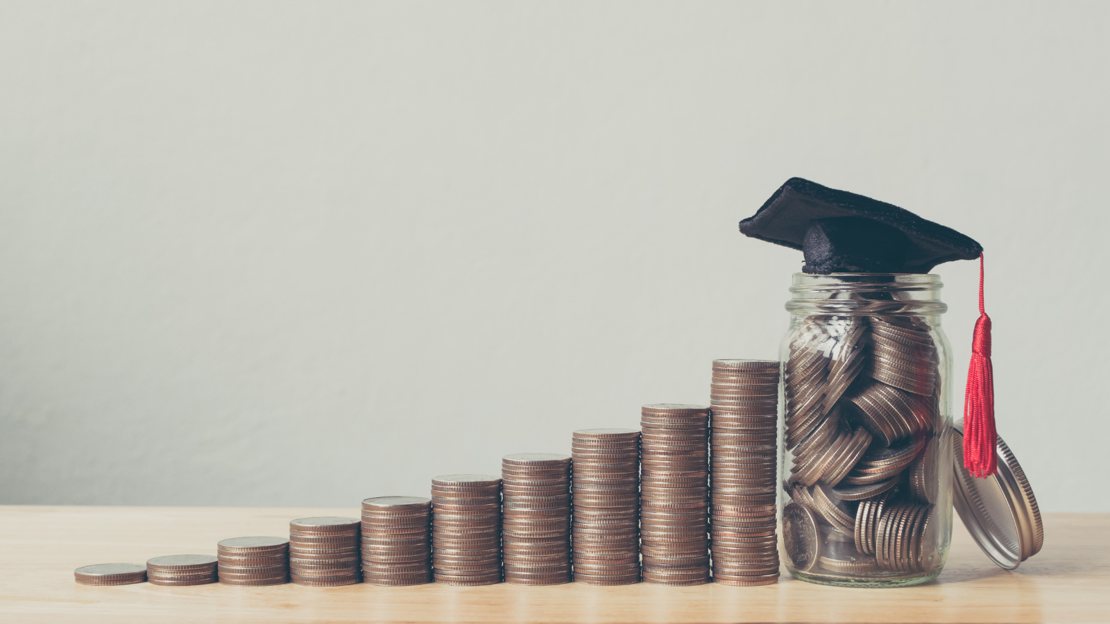 An image of coins next to a jar of coins with a grad cap on top.